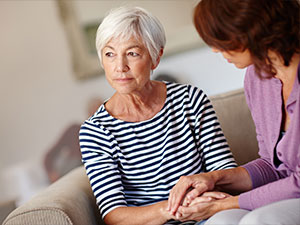 A senior lady looks into the distance as her caregiver holds her hand.
